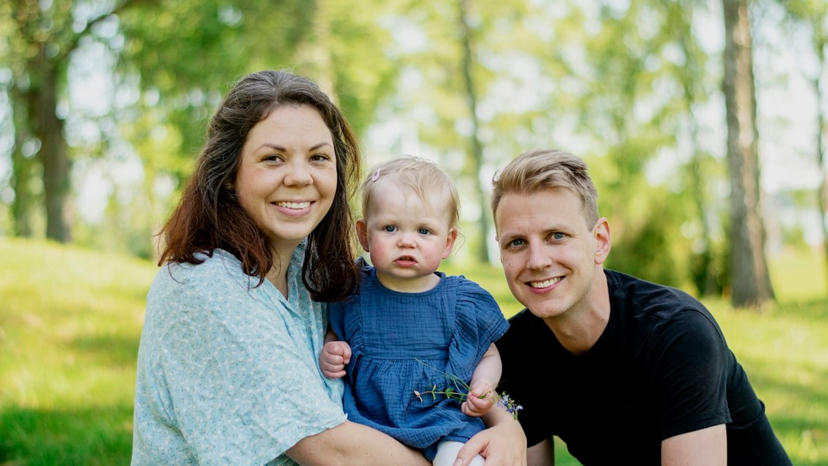 a man woman and child sitting on grass with trees in the background